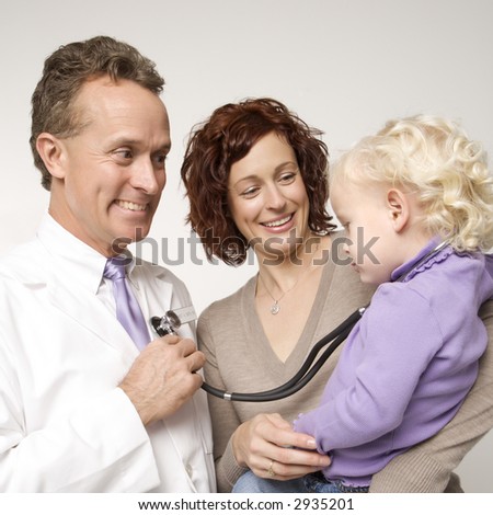 Caucasian female toddler with stethoscope around her neck as middle-aged male doctor holds it to his chest.