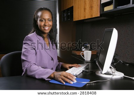 African-American young adult business woman working at computer in office smiling and looking at viewer.