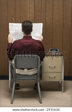 Back view of retro businessman sitting at desk reading paper.