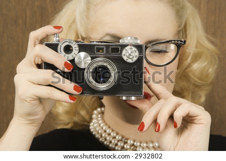 Mid-adult Caucasian female in vintage outfit holding a vintage film camera up to her face.