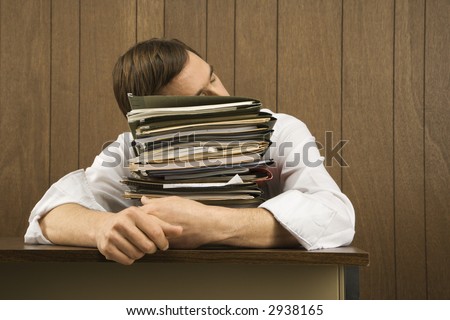 Man resting head on stack of paperwork.