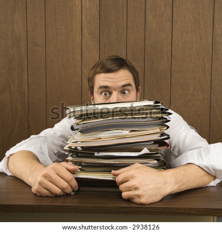 Mid-adult Caucasian male peeking over big stack of paperwork.