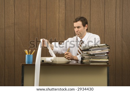 Mid-adult Caucasian male holding printout from calculator in office setting.