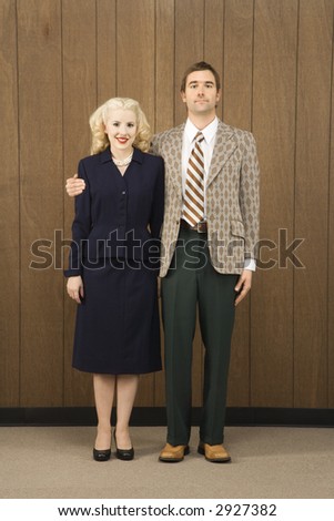 Mid-adult Caucasian male in retro suit with arm around mid-adult Caucasian female.