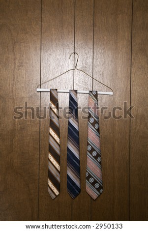 Three retro ties hanging on a wire hanger against wood paneling.