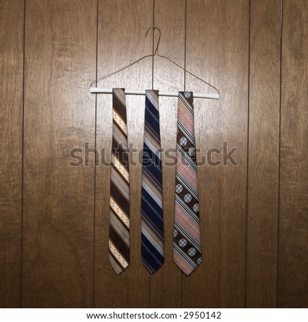 Three retro ties hanging on a wire hanger against wood paneling.
