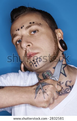  mid-adult man with tattoos and piercings holding knife to throat