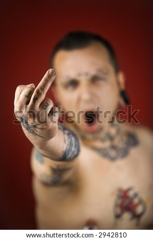 midadult man with tattoos and piercings holding up middle finger