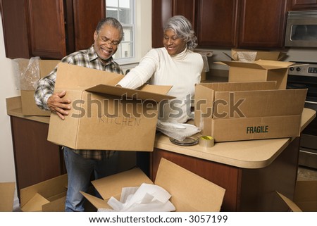 Middle-aged African-American couple packing moving boxes in kitchen.