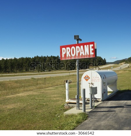 Propane tank with sign on side of rural road.