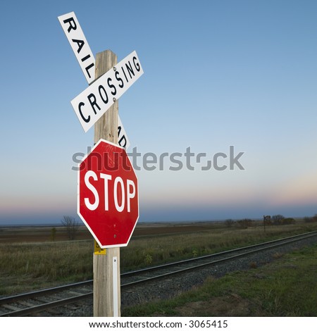 Railroad crossing and stop signs beside railroad tracks in rural setting.