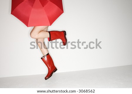 Legs of young Caucasian woman in red boots holding red umbrella and jumping.
