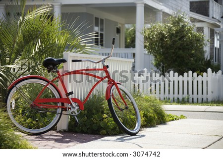 Red beach cruiser bicycle propped against fence in front of house.