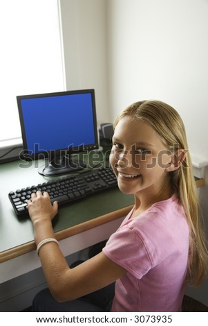 Caucasian pre-teen girl at computer looking over shoulder smiling at viewer.