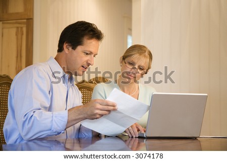 Caucasian mid-adult couple paying bills on laptop computer.