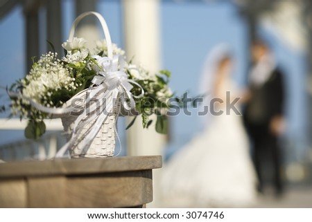 Flower basket with Caucasian bride and groom blurred in background.