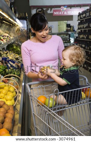 Caucasian mid-adult woman grocery shopping for fruit with young male toddler.