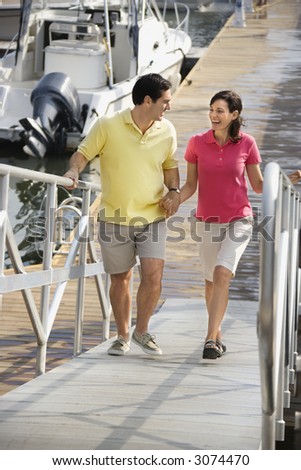 Mid-adult Caucasian couple holding hands and walking up ramp at harbor.