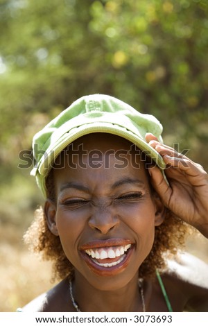 MId-adult Black female smiling with hand on cap and squinted eyes.