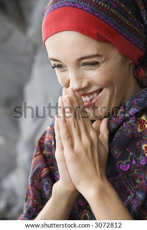 Caucasian young adult woman with hands together in prayer position holding up to face and smiling.