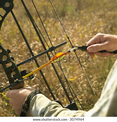Bow hunter hands holding compound bow in field.
