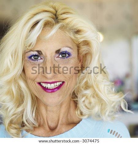 Portrait of tan blonde Caucasion middle-aged woman wearing lots of makeup smiling at viewer.
