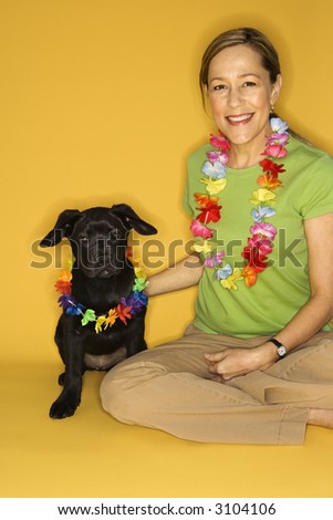 Caucasian prime adult female sitting with black puppy wearing leis.