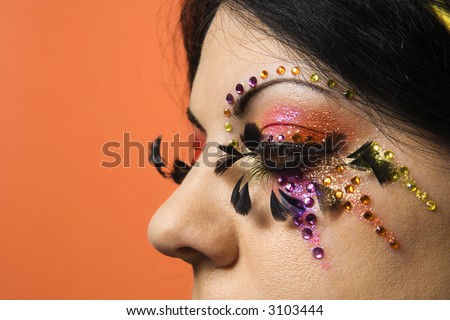 Close-up of Caucasian woman in unique makeup against orange background.