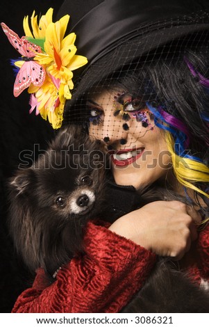 Caucasian adult in unique makeup and clothing holding black Pomeranian dog.