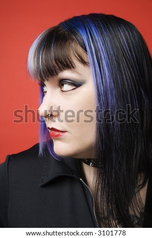 Portrait of Caucasian woman with blue hair, tattoo, and spike collar looking to side against orange background.