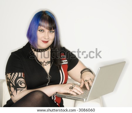 Portrait of Caucasian woman with blue hair, tattoo, and spike collar typing.