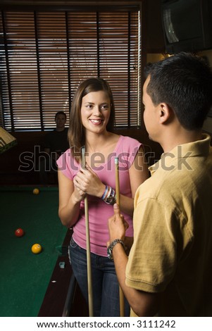 Young man and woman talking and smiling while playing billiards.