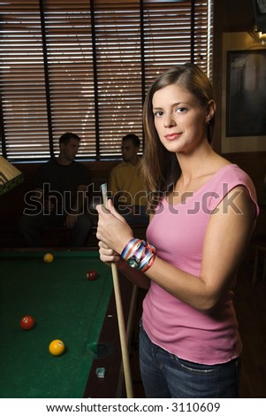 Portrait of woman standing by billiards table holding pool stick.