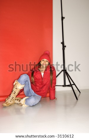 Portrait of Asian-American teen girl in studio setting sitting on floor next to light stand.