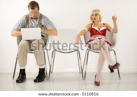 Caucasian young man dressed like nerd sitting with laptop with Caucasian young blonde woman looking at him.