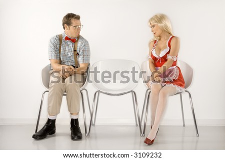 Caucasian young man dressed like nerd and Caucasian young blonde woman in french maid outfit sitting and looking at eachother.