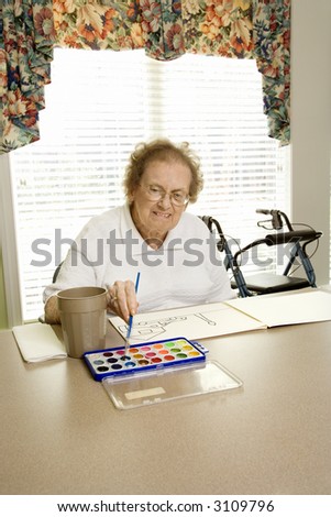 Elderly Caucasian woman painting with watercolors at retirement community center.