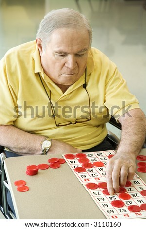 Elderly Caucasian man sitting in wheelchair playing bingo at retirement community center.