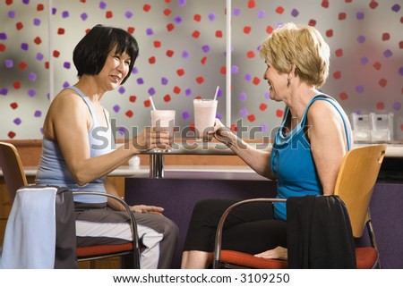 Mature Asian and Caucasian adult females sitting at table in health club cafeteria.