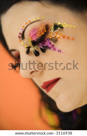 Close-up portrait of Caucasian woman in unique makeup with eyes closed against orange background.