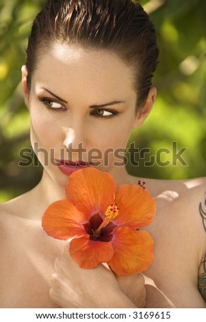Attractive nude Caucasian tattooed woman holding Hibiscus flower in Maui, Hawaii, USA.