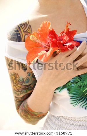 Caucasian tattooed woman holding Hibiscus flowers in Maui, Hawaii, USA.