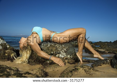Pretty Caucasian mid adult woman bodybuilder in bikini lying on rock on Maui beach.