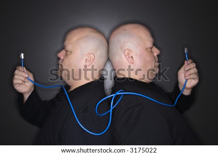 Caucasian bald mid adult identical twin men standing back to back holding ethernet cable.