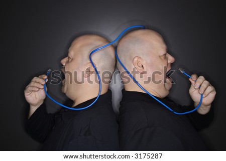 Caucasian bald mid adult identical twin men standing back to back yelling into ethernet cable.