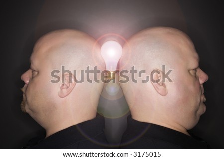 Caucasian mid adult identical twin men standing back to back and balancing a lightbulb between them.