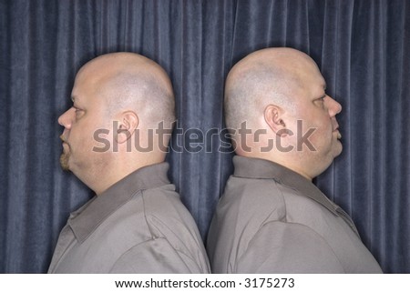 Profile of Caucasian bald identical twin mid adult men standing back to back.