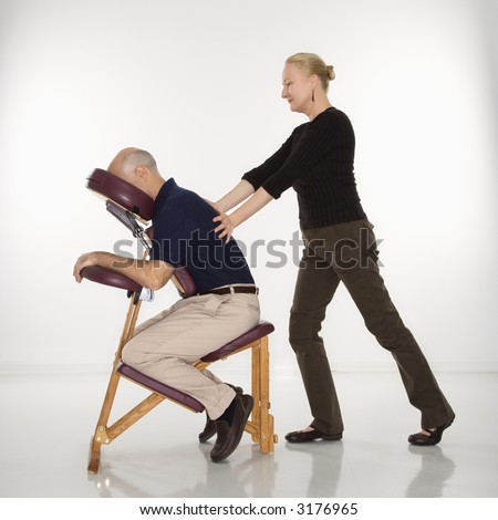 Caucasian middle-aged female massage therapist massaging back of Caucasian middle-aged man sitting in massage chair.