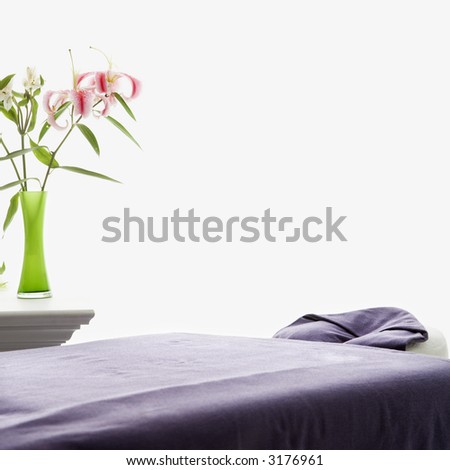 Spa scene of massage table with purple sheets and table with pink Easter lillies in green vase.