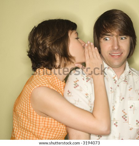 Pretty Caucasian mid-adult woman whispering into Caucasian mid-adult man\'s ear with surprized expression on face.
